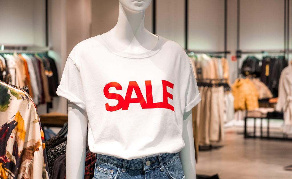 mannequin wearing a white t-shirt with the word SALE in red black capitals.  Out of focus womenswear in the background